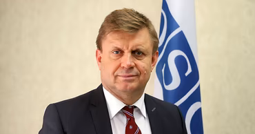 Portrait of Valeriu Chiveri, Moldovan diplomat, standing in front of an OSCE flag.