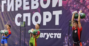 Young athletes competing in a kettlebell lifting tournament in front of a branded backdrop.