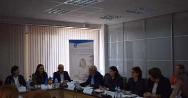 A group of people sitting at a conference table with an ANOFM banner in the background.