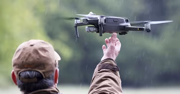 A person holding a drone in the air outdoors.