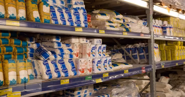 Shelves in a supermarket stocked with various packages of white sugar.