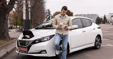 A man standing next to a white electric car charging at a station.