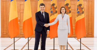 Nicușor Dan and Maia Sandu shaking hands in front of Moldovan flags.