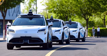 A convoy of white autonomous self-driving cars driving on a road.