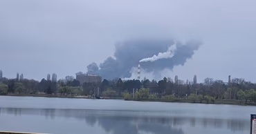 A large plume of dark smoke rising over a lake in Chisinau during a fire.