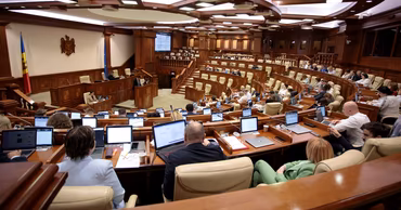 A wide shot of the Moldovan Parliament session hall with deputies working at their desks.