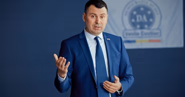 Vasile Costiuc in a blue suit speaking in front of a party banner.