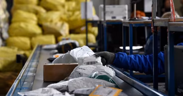 A worker sorting parcels on a conveyor belt in a logistics facility.
