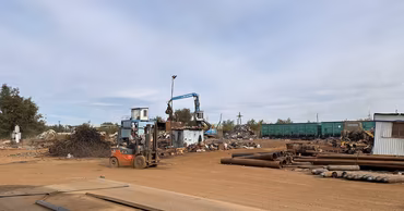 A forklift operating at a scrap metal collection yard with piles of metal pipes.