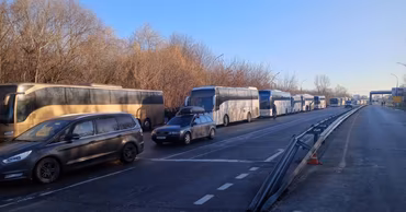 A line of buses and cars waiting at a border crossing point.