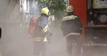 Two Moldovan firefighters in uniform standing near a fire truck in a smoky environment.