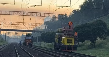 Railway tracks with maintenance vehicles and workers at sunset.