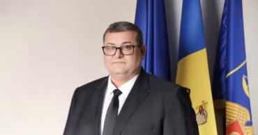 A man in a suit standing in front of the Moldovan flag.
