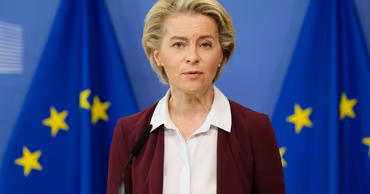 Ursula von der Leyen speaking at a podium with European Union flags in the background.