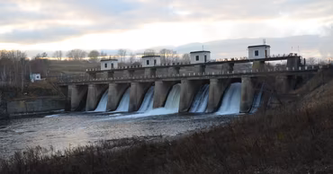 A concrete dam with water flowing through its spillways under a cloudy sky.