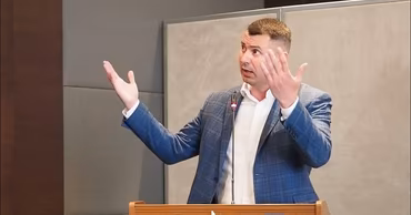 Dinu Plîngău speaking at a podium during a press conference.