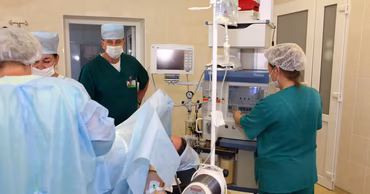 Medical staff in scrubs working with anesthesia equipment in a hospital operating room.