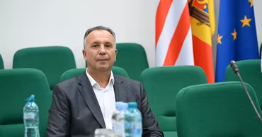 Emil Ceban sitting at a table with Moldovan and EU flags in the background.