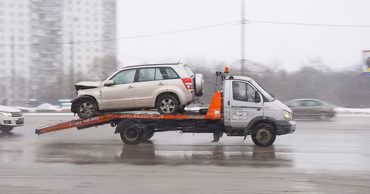 A damaged SUV being transported on a tow truck on a city road.