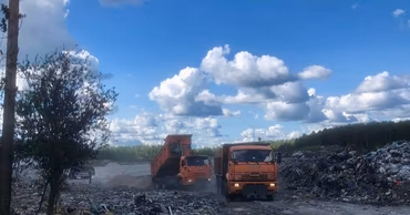 Orange dump trucks operating at a large landfill site under a blue sky.