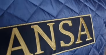 Close-up of the ANSA logo embroidered on a blue quilted jacket.