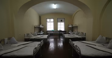 A view of a sparse prison cell with multiple beds and barred windows.