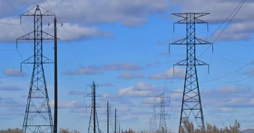 High-voltage electricity transmission towers standing in a field under a blue sky.