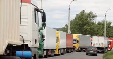 A long line of heavy trucks waiting on a road near a border crossing.