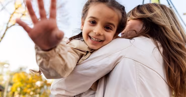 A smiling young girl being held by an adult, representing adoption and family care.