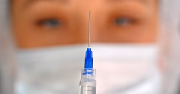 A medical professional in a mask holding a syringe with a vaccine.