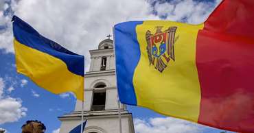 Flags of Moldova, Ukraine, and the European Union waving in front of a church tower.