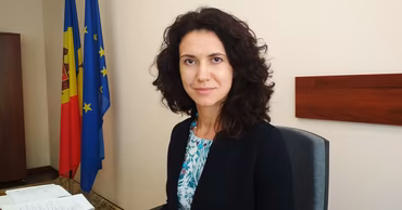 Olesea Stamate sitting at a desk with Moldovan and European Union flags in the background.