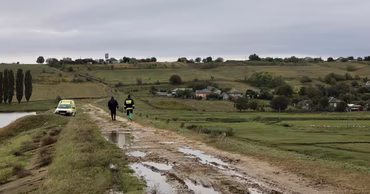 Two environmental inspectors walking on a muddy path near a river in a rural area.