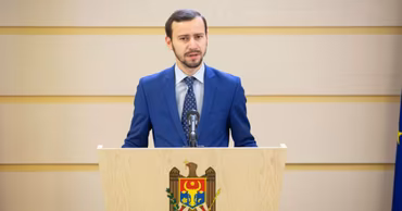 Dinu Plîngău speaking at a podium with the Moldovan coat of arms.