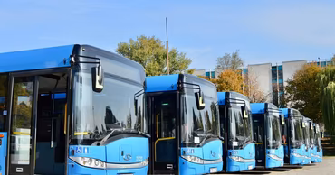 A row of blue public transport buses parked in a lot.
