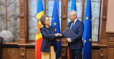 Two officials shaking hands in front of Moldovan and European Union flags during a formal meeting.