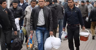 A group of male migrants walking on a train platform carrying bags and belongings.