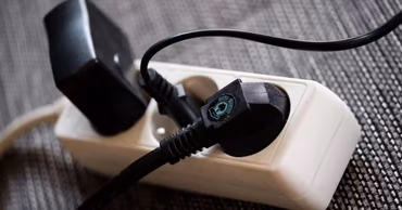 A white power strip with several black electrical plugs inserted into it.