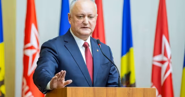 Igor Dodon speaking at a podium with Moldovan and party flags in the background.