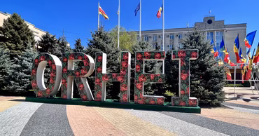 A decorative sign spelling ORHEI in a public square with flags in the background.
