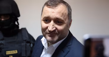Vlad Filat in a suit with a security officer in the background.