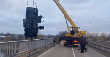 A crane lifting a wrecked car from a bridge after a fatal accident in Moldova.