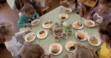 Children sitting at a table in a kindergarten eating their lunch.