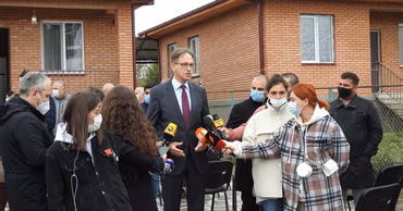 Hubert Knirsch speaking to a group of journalists holding microphones in an outdoor setting.