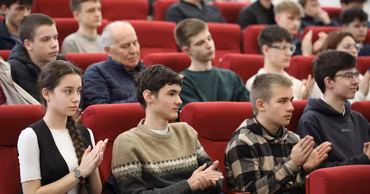 A group of young students sitting in a lecture hall and applauding during an academic event.