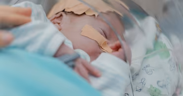 A newborn baby in an incubator receiving medical care.