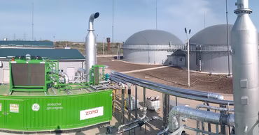 A modern biogas production facility with large industrial tanks and gas engine equipment.
