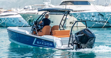 A person driving a modern motorboat on the water near a marina.