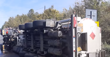 An overturned tanker truck lying on its side on the side of a road.
