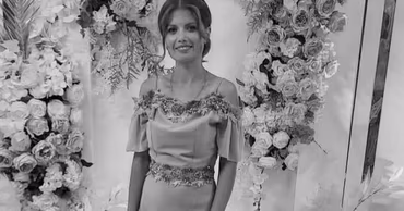 A black and white portrait of Ludmila Vartic standing in front of floral decorations.